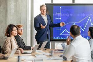 A confident businessman in a blue suit stands in front of a large screen displaying a blue and white graph. The graph shows a strong upward trend with a rising line, suggesting positive growth photo