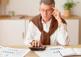 Pensive Senior Man Using Calculator Working Sitting In Modern Office. Getting Ready For Retirement. Selective Focus photo