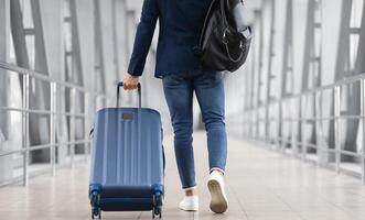 Unrecognizable Man With Bag And Suitcase Walking In Airport Terminal, Rear View Of Young Male On His Way To Flight Boarding Gate, Ready For Business Travel Or Vacation Journey, Cropped, Copy Space photo