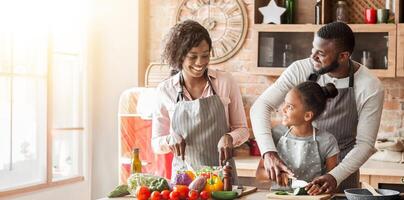 African american man teaching daughter how to cut vegetables, mom making salad, talking while cooking in kitchen, free space photo