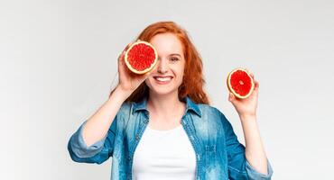 A woman is holding two pieces of grapefruit up to her eye, seemingly as a playful and quirky gesture. She appears to be enjoying the moment and exploring the textures and colors of the fruit. photo
