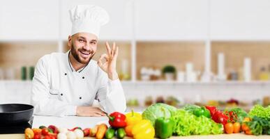 Professional Chef. Smiling Cook Man Gesturing Okay Sign Standing Next To Work Table In Restaurant Kitchen Indoor photo