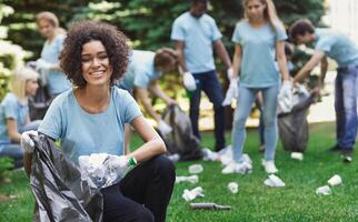 Volunteering, charity and clean environment concept. Happy black woman and group of volunteers with garbage bags cleaning area in park, copy space photo
