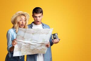 Young couple of tourists holding a map being shocked, cause they mixed their route. Yellow background with empty space photo