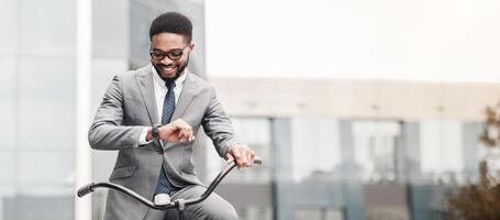 African American professional in a suit is on a bicycle, looking at his watch in the city. The atmosphere is dynamic and fast-paced, capturing the essence of urban commuting and punctuality. photo