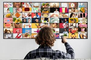 A young person is seated in a living room watching a screen displaying a large grid of colorful images. The images on the screen are diverse, featuring a variety of people, objects, and scenes. photo