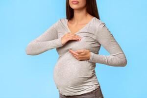 Sore Breasts. Unrecognizable Pregnant Lady Suffering From Pain Touching Chest Standing Over Gray Studio Background. Cropped photo
