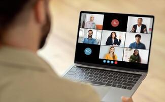Man using a laptop while a group of people are visible on the screen. The person is engaged in virtual communication or collaboration with the individuals displayed on the laptop screen. photo