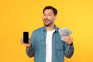 A man is shown in the image holding a stack of money in one hand and a cell phone in the other hand. He appears to be engaged in a financial transaction or communication involving money. photo