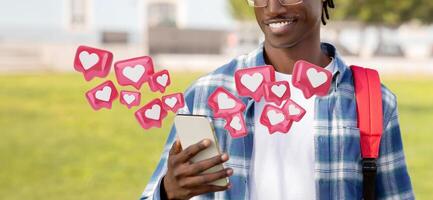 Cropped of young black man wearing a plaid shirt and a backpack is using his smartphone outdoors. He is smiling and looking at his phone screen. Digital hearts are floating around him photo