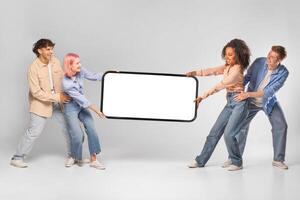 Four young adults, two men and two women, stand in a studio, holding up a blank white rectangular sign. They are all dressed casually and are looking at the camera with smiles on their faces. photo