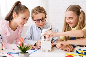 Three children, a boy and two girls, are working together on a robotics project in a classroom setting. They are all focused on the project, and they appear to be enjoying themselves photo