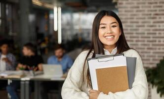Happy girl in modern library smiling to camera, classmates studying on background in high school university photo