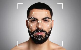 Middle eastern man is undergoing facial recognition analysis, with pattern mapping visible on his face against a neutral background. photo