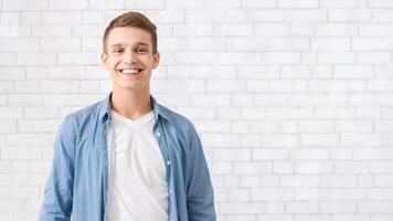 Portrait of handsome smiling guy posing over white brick wall photo