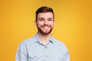 Young handsome man with a beard smiling directly at the camera in a close-up shot, posing isolated on yellow studio background photo