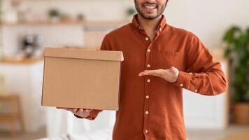 Cropped of smiling man in a red shirt holds a cardboard box in front of him, his other hand extended towards the viewer. The background is blurred, creating a soft and inviting atmosphere. photo