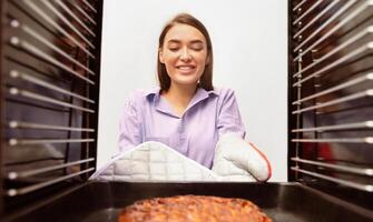 Happy household. Cheerful housewife removing tasty pie from oven, view from inside photo