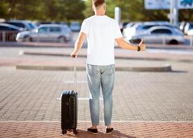 Arriving Home Concept. Tourist trying to catch taxi, standing with baggage and showing thumbs up, copyspace, back view photo