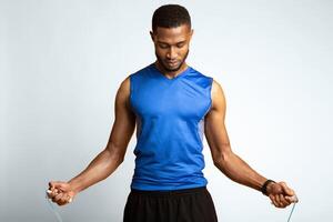 Workout. Afro sports man in sportswear exercising with skipping rope, jumping at studio over yellow background, warm up photo