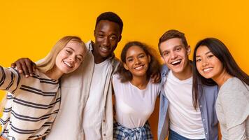 Friendly international students embracing and taking selfie over yellow background photo
