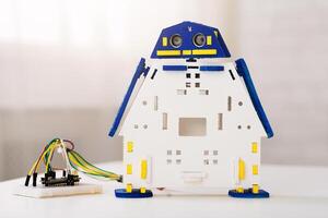 An unassembled white and blue robot kit with a yellow and blue ultrasonic sensor. The robot kit is assembled in the form of a house and is sitting on a white table photo