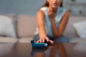 Unrecognizable Girl Reaching For Asthma Inhaler Preventing Attack Sitting On Sofa Indoor. Selective Focus, Shallow Depth photo