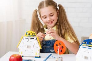 A young girl with pigtails is sitting at a table, intently building a robot toy. She is connecting wires and gears, showing focus and concentration as she works. photo
