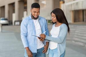 Exit poll concept. Female interviewer making voter survey outdoors after election, talking with young african american guy and taking notes photo