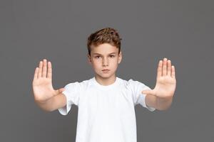 This image showcases a teenager standing isolated with a serious expression, making a stop gesture with his open palms photo