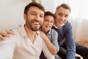 Male generations. Happy adult man with son and elderly father making selfie smiling sitting on sofa at home. photo