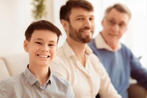Male Family. Cheerful Boy With Father And Grandfather Smiling At Camera Sitting On Couch At Home. Shallow Depth photo