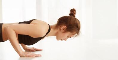 A woman dressed in a black top is engaged in a push-up exercise, demonstrating strength and determination. Her body is extended in a straight line, showcasing proper form and muscle engagement. photo