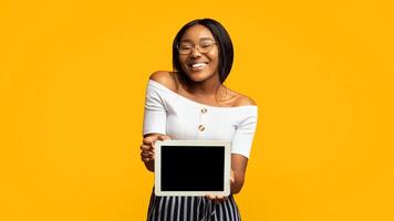 Great Application. Smiling Afro Girl Showing Digital Tablet With Blank Screen Standing In Studio Over Orange Background. Panorama, Mockup photo