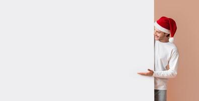 Cheerful Interracial Couple In Santa Hats Pointing At White Billboard With Free Space For Advertisement Or Text, Yellow Background photo