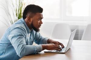 Working on new project. Concentrated young african worker using laptop in office, side view with free space photo