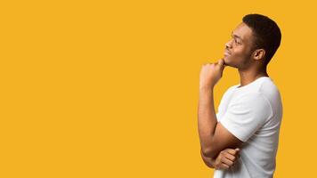 Making Decision. Side view of black guy looking at copy space, thinking about purchase, panorama, orange background photo