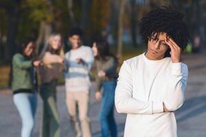 Multiracial group of teenagers pointing at frustrated black guy, spending time in park photo
