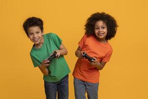 Two African American young children, a boy and a girl, stand side by side with big smiles, each holding a game controller, yellow background photo