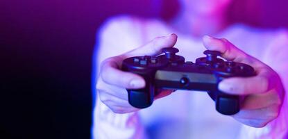 A woman is seen holding a game controller in front of a vibrant purple light, engaged in a gaming session. The controller is illuminated by the vivid purple glow, creating a striking contrast. photo