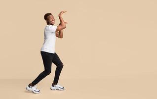 Funny Black Guy Dancing In Egypt Style Having Fun And Fooling Over Orange Studio Background. Free Space For Text photo