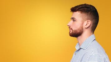 Side view of redhaired man with a beard wearing a striped shirt posing isolated on yellow studio background, panorama with copy space photo