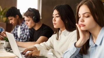 Diverse students sitting at college library, making notes, using laptop and doing homework photo