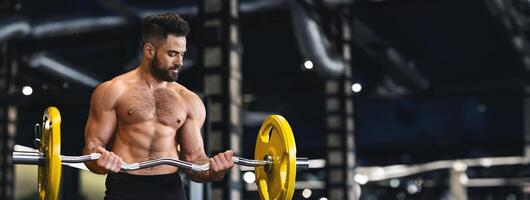 A muscular man performs a bicep curl with a barbell in a well-equipped gym, focusing on his workout, copy space photo