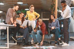 A diverse team discusses and reviews project materials spread on the floor in a modern office, engaging in a collaborative brainstorming session. photo