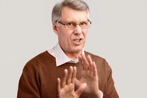 Disgust. Disgusted Senior Man Gesturing No Disapproving Something Posing On Gray Background. Studio Shot photo