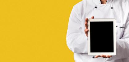 Unrecognizable Chef Man Showing Empty Tablet Screen Recommending Menu Or Food Delivery App Standing Over Black Background. Cropped, Mockup, Panorama photo