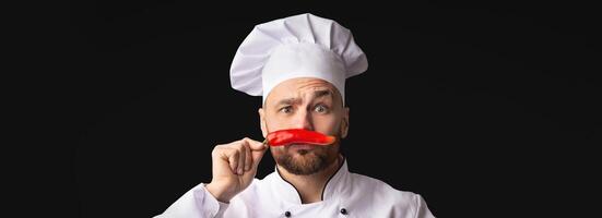 Chef Man Having Fun Posing With Red Chilli Pepper Holding It Like Moustaches Standing On Black Background. Panorama, Copy Space photo