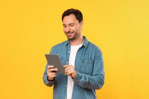 Guy wearing a blue shirt is engrossed in using a tablet device. He is focused on the screen, possibly reading or viewing content photo