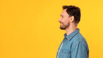 A man is standing in front of a bright yellow background. He is facing forward with a neutral expression. The background color contrasts sharply with his dark-colored clothing, copy space photo
